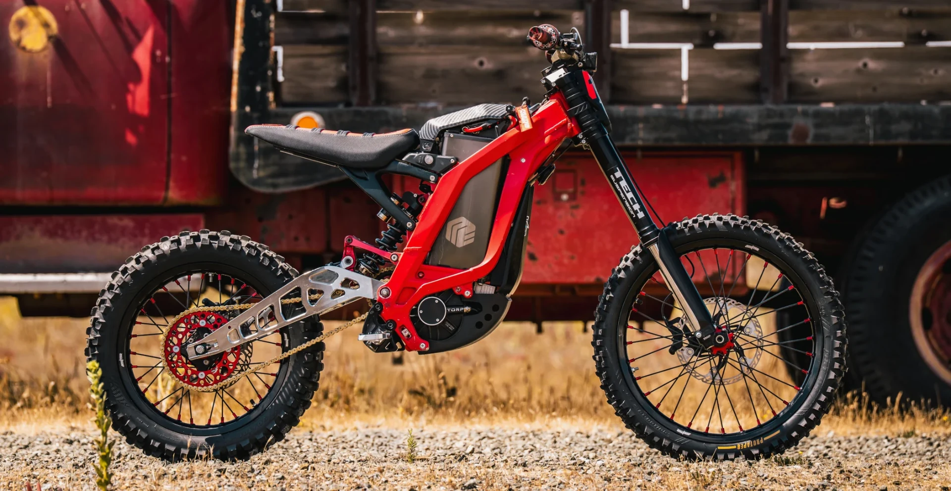 Red Sur-Ron electric dirt bike parked in front of a weathered red barn
